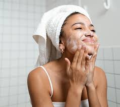 Woman washing her face in the shower as part of a well hydrated skincare routine